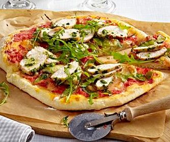 Chicken and rocket pizza on a wooden board with a pizza cutter